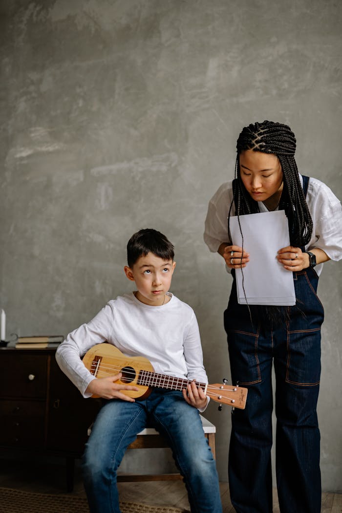 Boy learning ukulele with music teacher guidance, indoors setting.