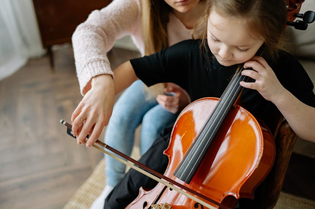 A child learning to play the cello with teacher guidance in a cozy indoor setting.