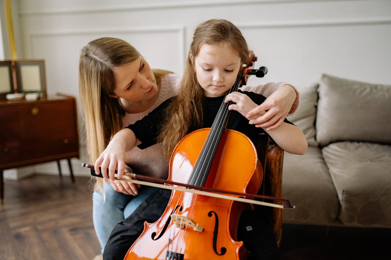 A young girl receiving cello lessons from a teacher in a cozy living room setting.