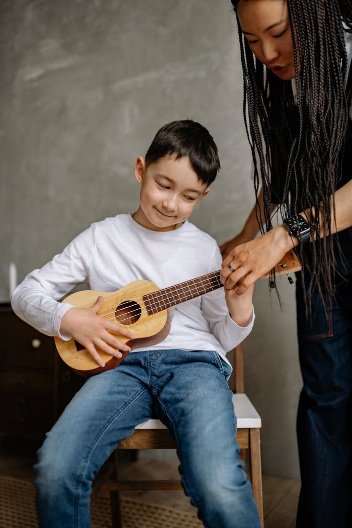 A young boy receives a ukulele lesson from a music teacher indoors.
